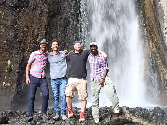 Four members of the team standing in front of a waterfall in Arusha National Park in 2026.